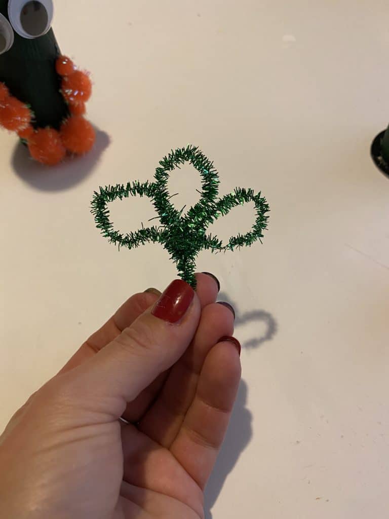 Bend a green pipe cleaner to make a shamrock for the paper tube leprechauns hat.