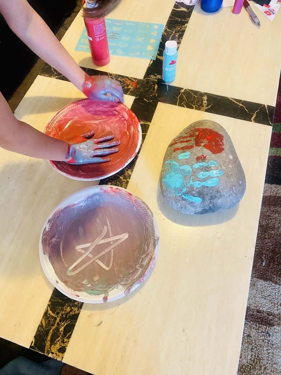 Kids dipping their hand in the paint to make the hand print for the rock.