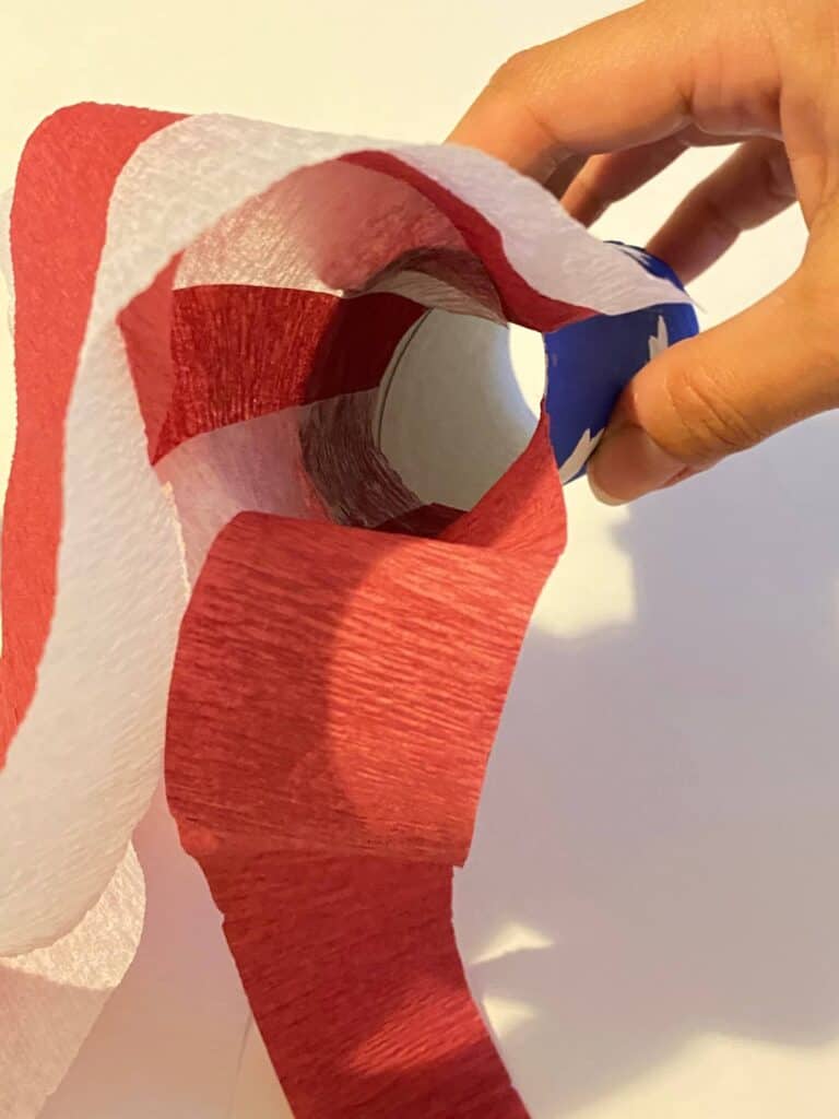 Glue the red and white streamers to the inside of the blue painted toilet paper tube