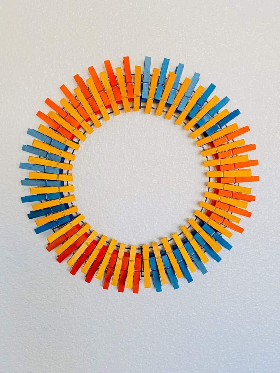 Continue this pattern of one section orange, one section blue, with yellow going continuously around, until you have the entire wreath form covered in clothespins
