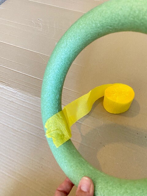 Put a small dab of glue on the end of the yellow crepe paper and adhere it to the foam wreath in a diagonal fashion