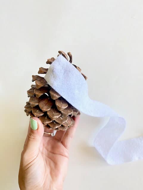 Cut the white felt into long thin strips to serve as the wrap for the pine cone mummy.