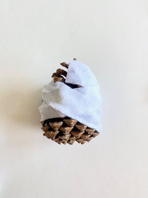 Put a dab of glue on the felt, and begin to wrap the felt around the pine cone. Wrap it in every which way all around.
