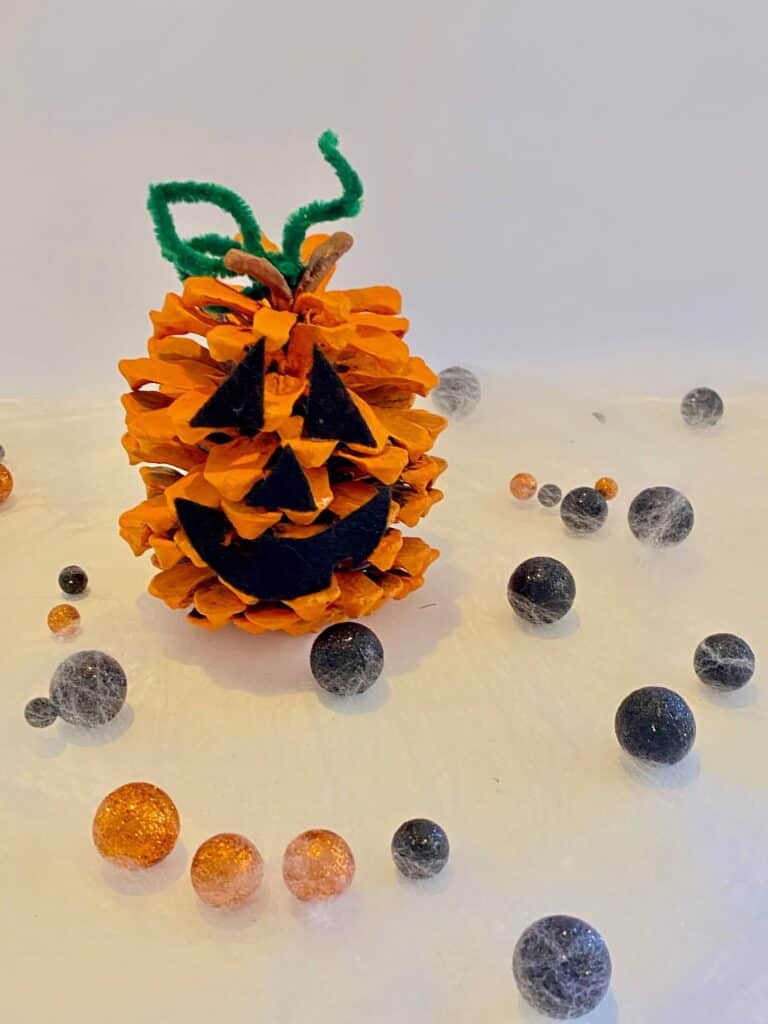 Completed pine cone pumpkin with a green pipe cleaner stem and black felt jack-o-lantern face..