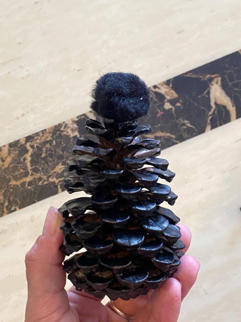 Glue the black craft pom pom to the top of the black painted pine cone