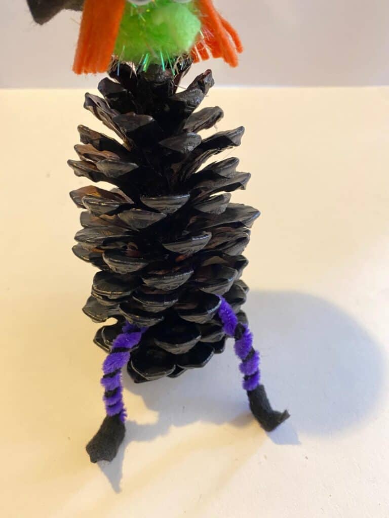 Glue the pipe cleaner legs to the bottom of the pine cone witch.