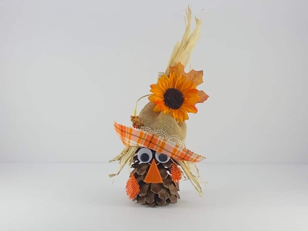 Complete the pine cone scarecrow craft by adding a sunflower and fall leaf embellishment to the hat. 