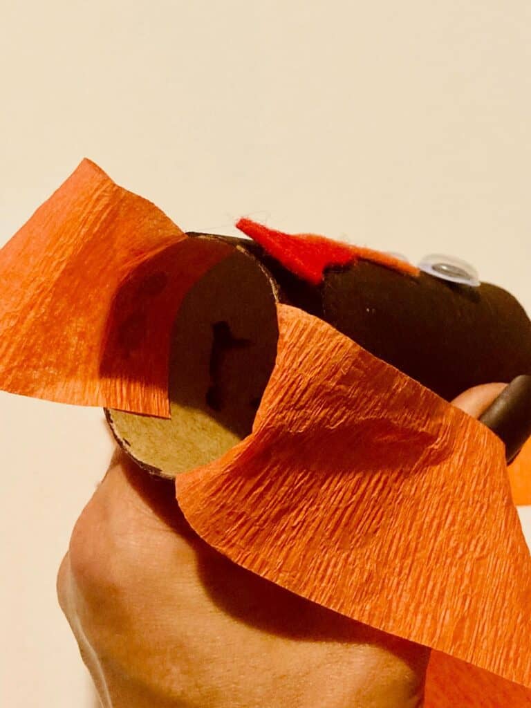 2 orange crepe paper streamers glued to the inside bottom of a brown painted empty toilet paper roll turkey face.