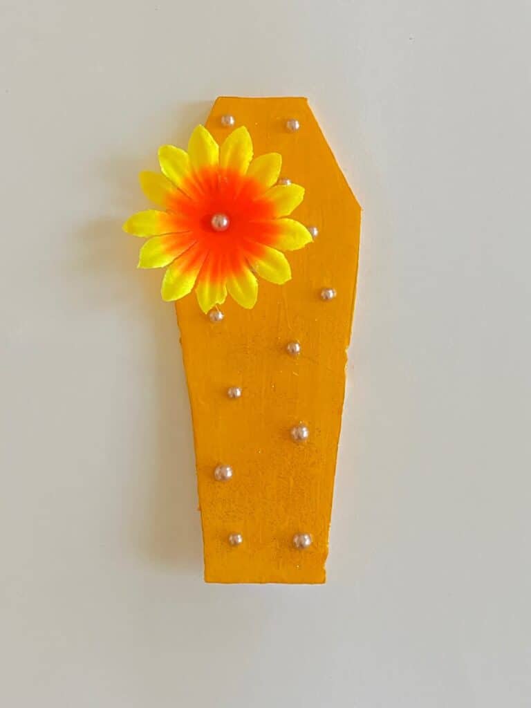 Yellow painted foam board coffin with cream yellow jewels as well as a yellow flower embellishment.