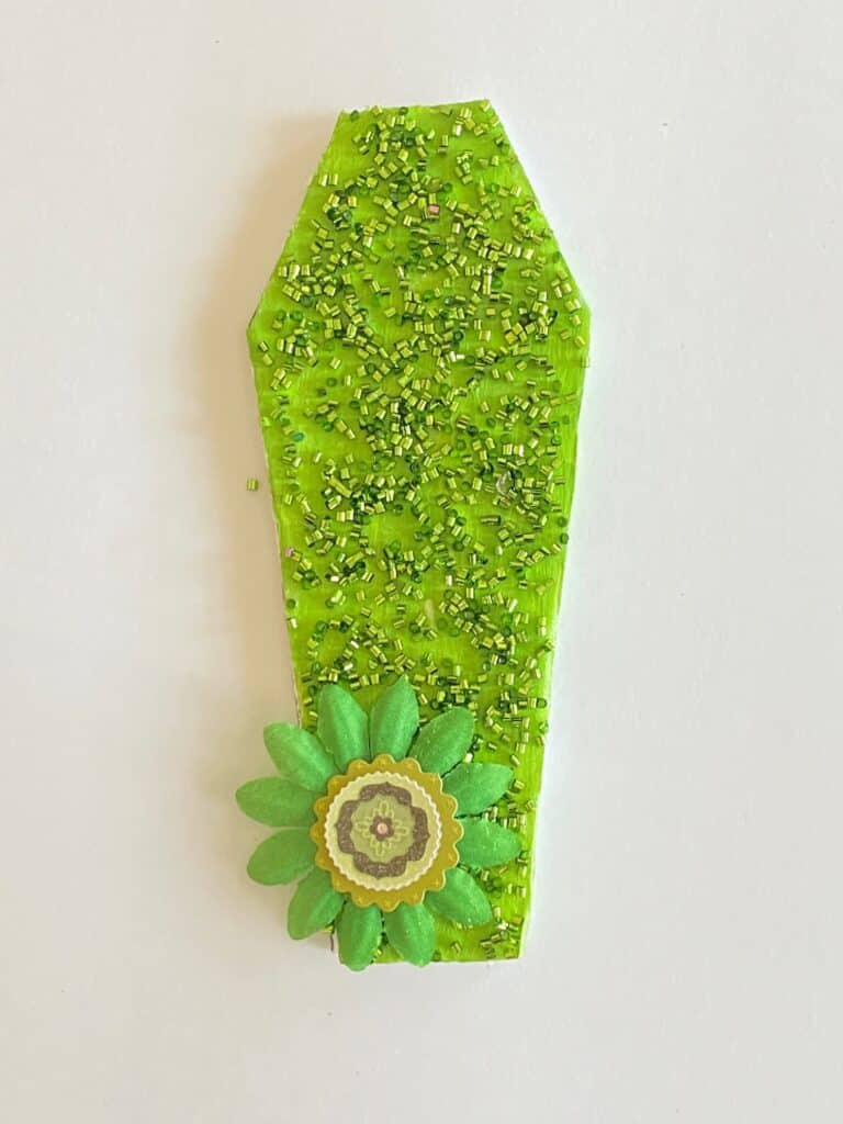 Green painted foam board coffin with green tube confetti as well as a green flower embellishment.