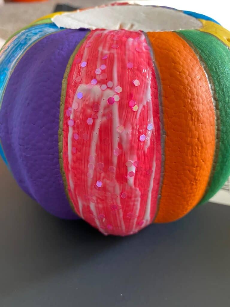 Add mod podge and glitter to the DIY rainbow painted dollar tree foam pumpkin.