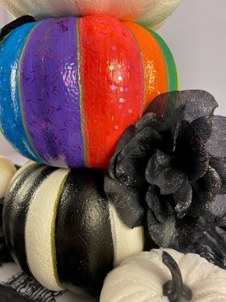 Glue the other black rose to the crease between the rainbow painted foam dollar tree pumpkin and the black and white striped bottom pumpkin on the right hand side.