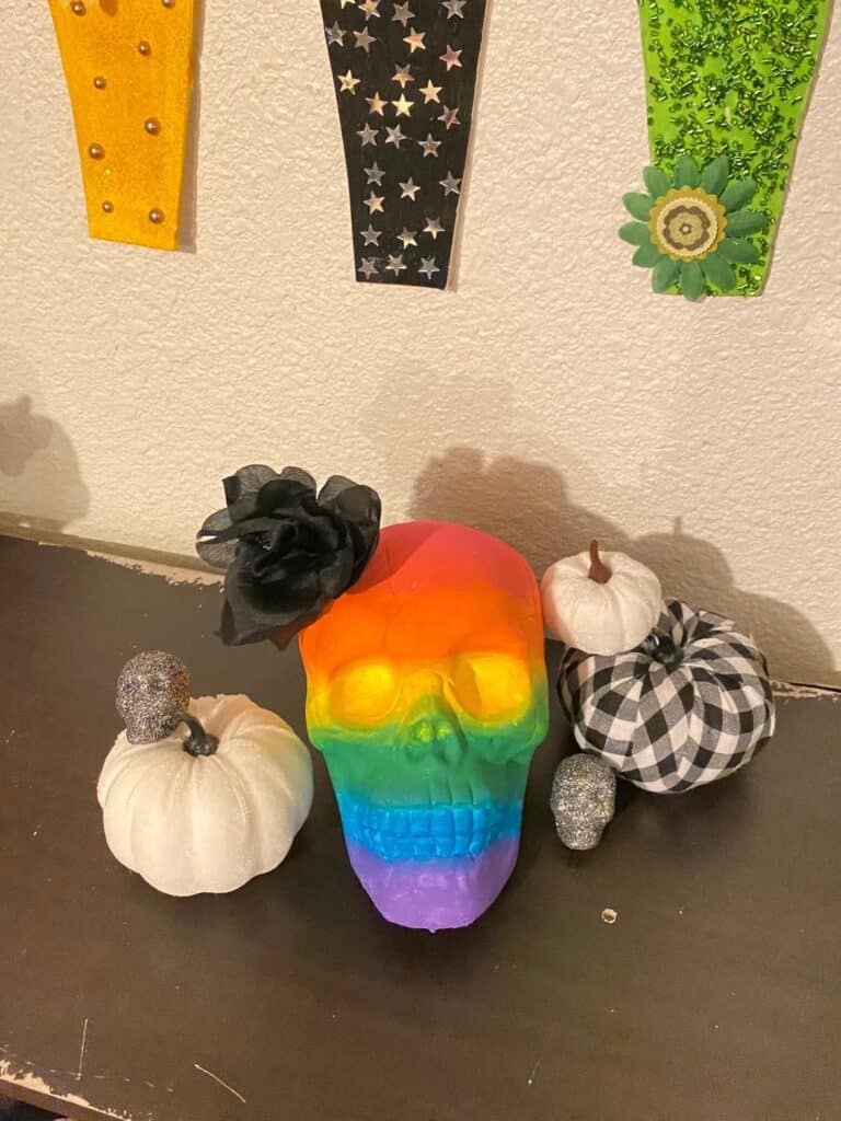 Dollar Tree Skull Makeover DIY. Rainbow Painted Ombre Skull with a black faux rose for Halloween party decor.