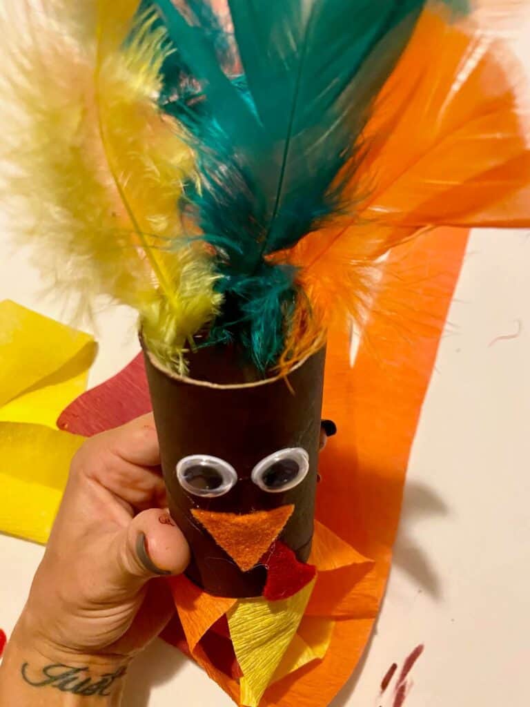 Feathers glued to the inside top of a brown painted toilet paper roll with a Turkey face glued on.