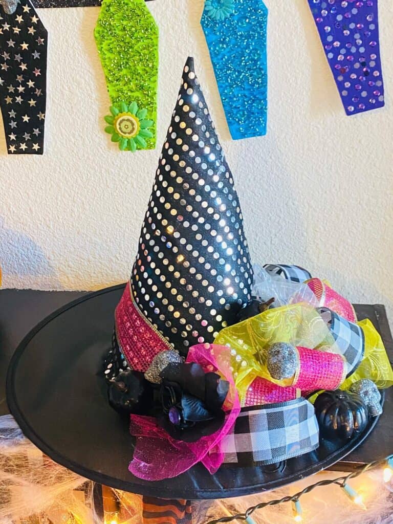 DIY Dollar Tree Glam Halloween Witch Hat Makeover. Witch hat with silver dots and pink ribbon with a faux black rose and yellow tulle.