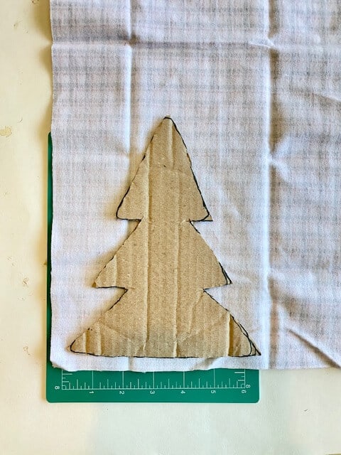 Cardboard christmas tree template on  on plaid fabric and cutting mat.