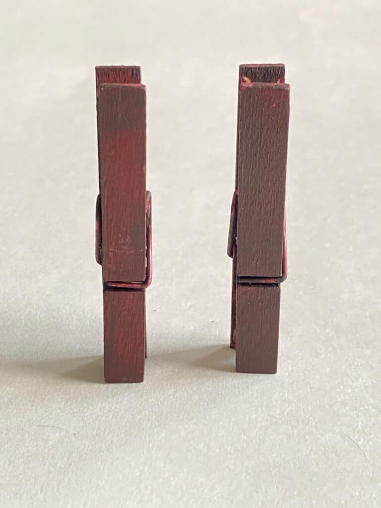 2 brown painted wooden clothespins.