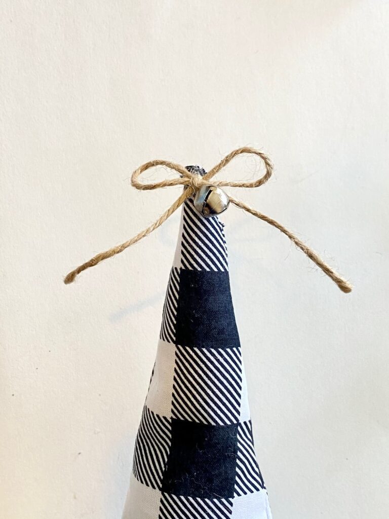 Small twine shoelace bow with a mini silver bell glued to the top of a buffalo check fabric christmas tree.