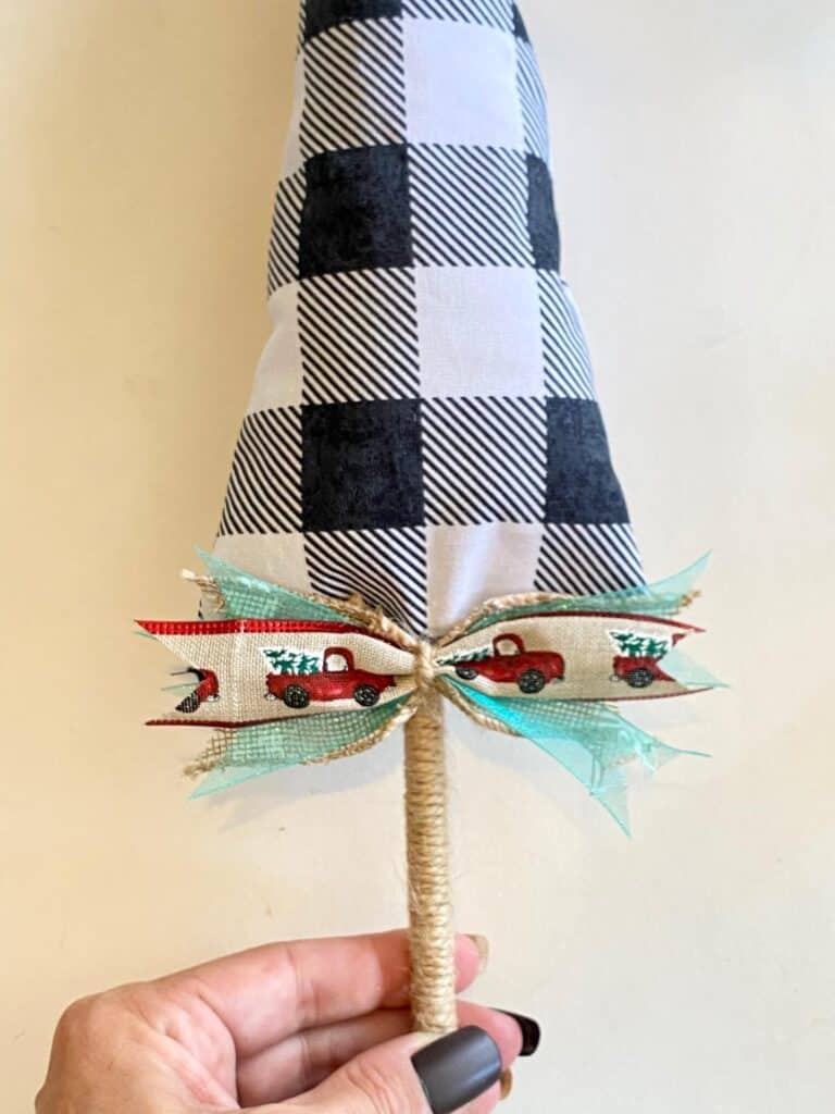 Glue the farmhouse scrap ribbon bow to the bottom of the buffalo check fabric Christmas tree where the bottom meets the twine covered wooden dowel.