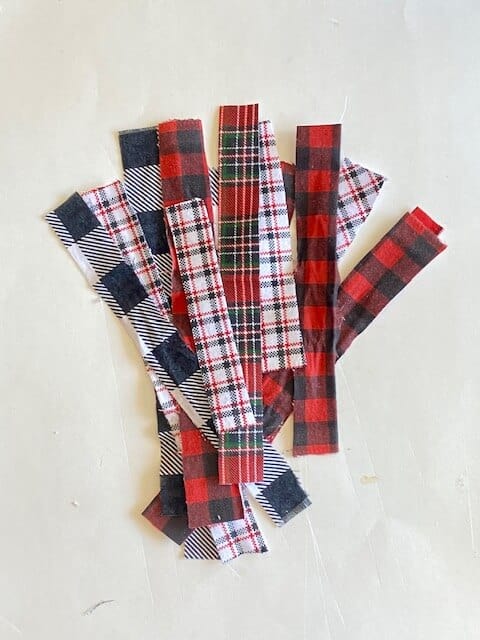 Long skinny strips of Christmas themed fabric from black and white buffalo check to red and black buffalo plaid, green and red plaid, and white grey and red plaid.
