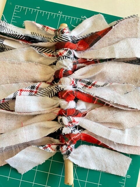 The back view of the strips of holiday pattern scrap fabric tied into knots around the wooden dowel.