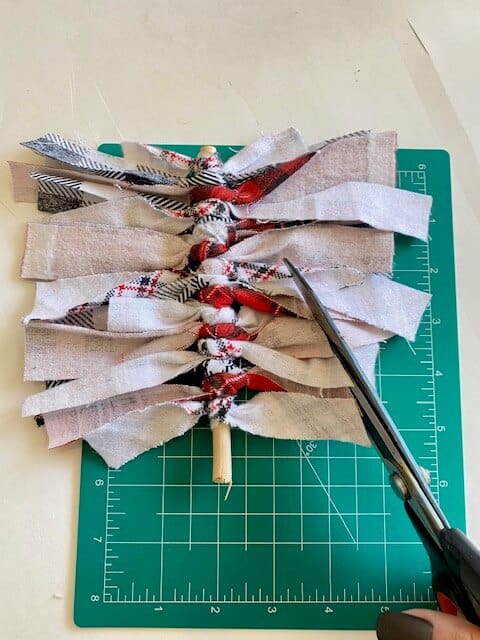Scissors cutting the scrap fabric tied strips into the shape of a Christmas Tree.