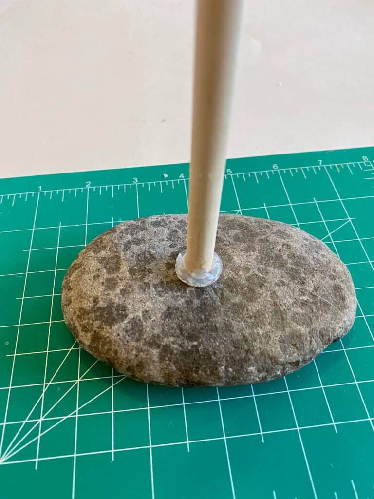 The end of a wooden dowel hot glued to a rock, on top of a green cutting mat.