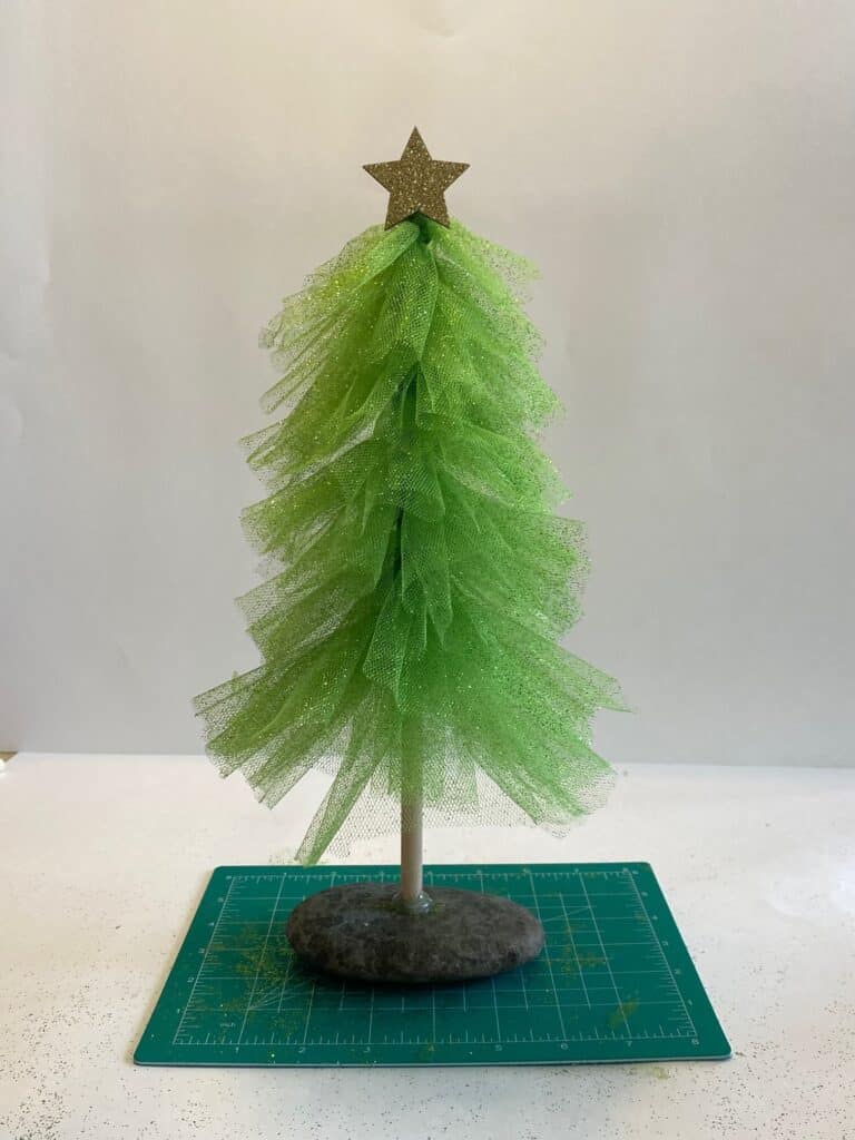 Completed green glitter tulle Christmas tree with tulle tied to a wooden dowel and the tree glued to a rock as the base with a yellow sparkly star on top.
