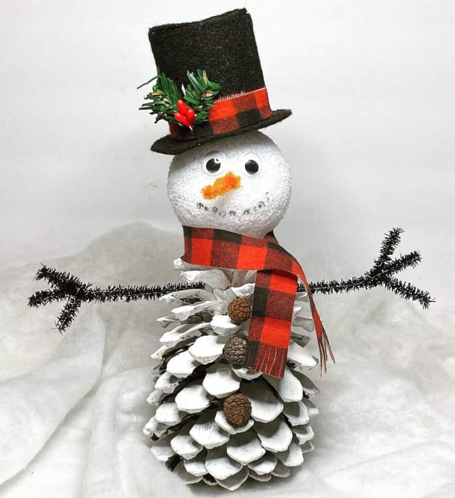 Pine Cone Snowman, christmas nature craft for kids with a top hat, carrot nose, and plaid scarf.
