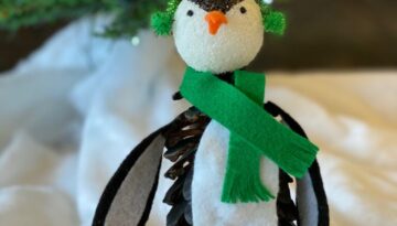 Pine Cone Penguin kids christmas nature craft with a winter scarf and earmuffs.