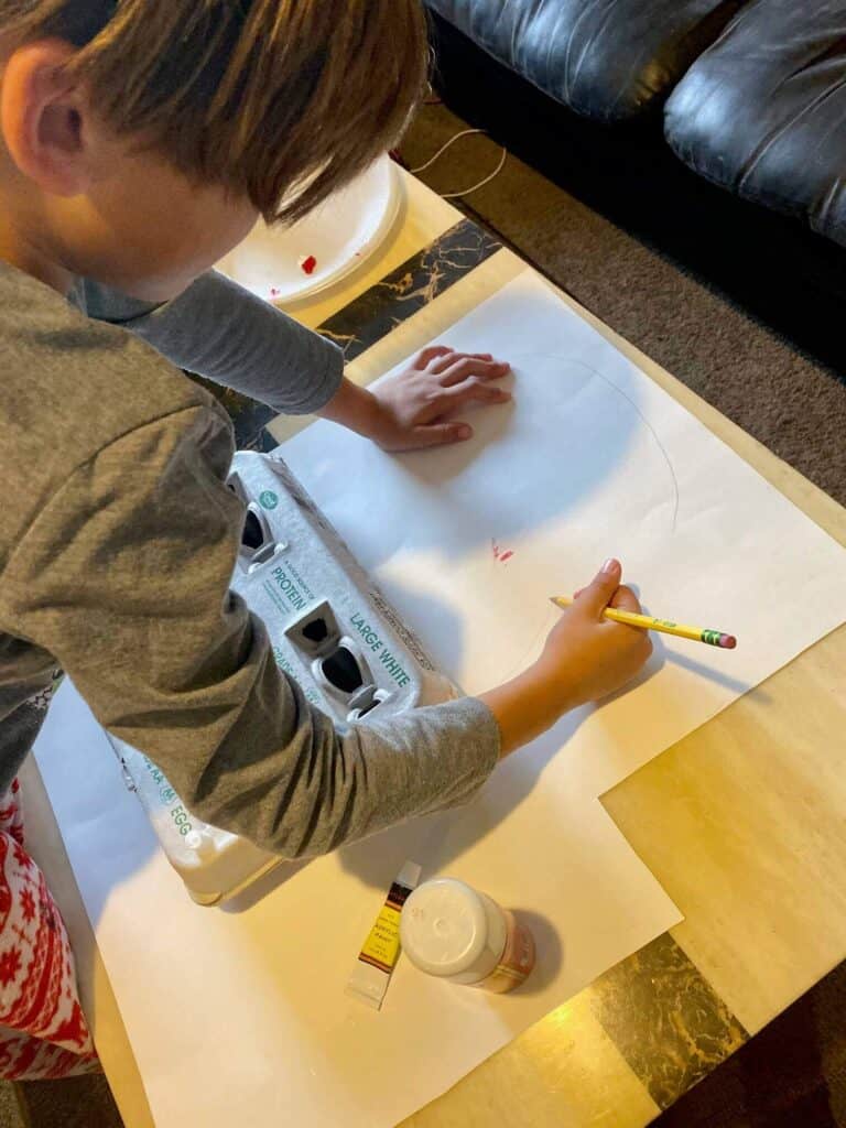 Back view of a child drawing the outline of Santa's face onto white foam board.