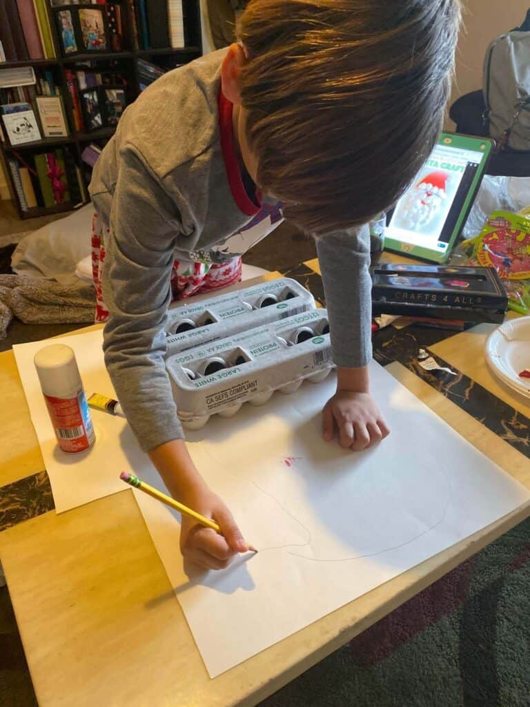 Front view of a Child drawing the outline of Santa's hat onto white foam board.