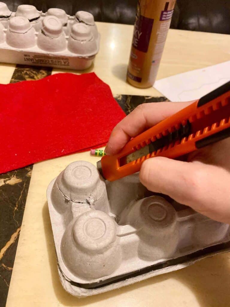 An Xacto knife cutting a 3/4 slit around the top of each egg cup to make a flap so that the candy can go into the advent calendar.