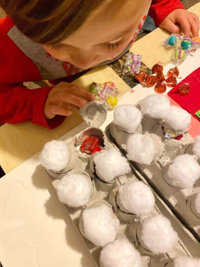 Child filling the egg carton cups with candy and chocolate for the advent calendar.
