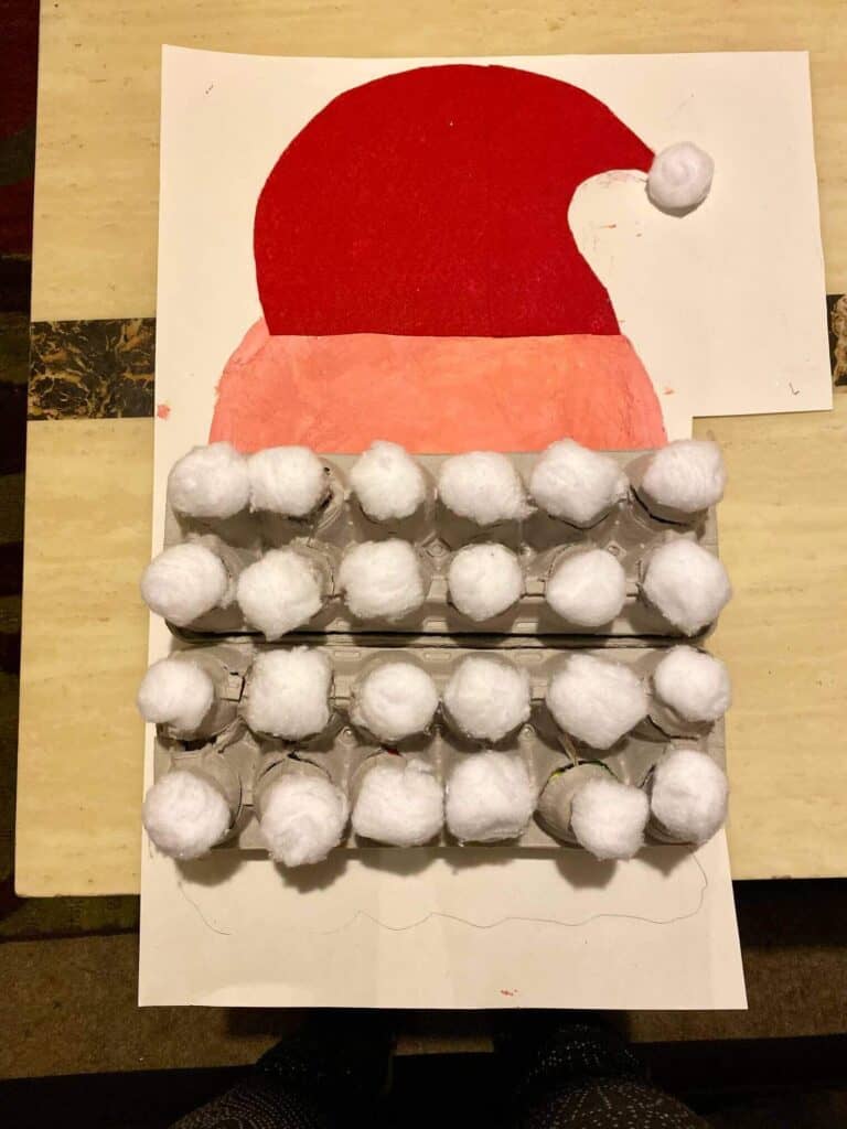 Glue the egg cartons with the cotton balls to the white foam board underneath santas head in place of there the beard would be.