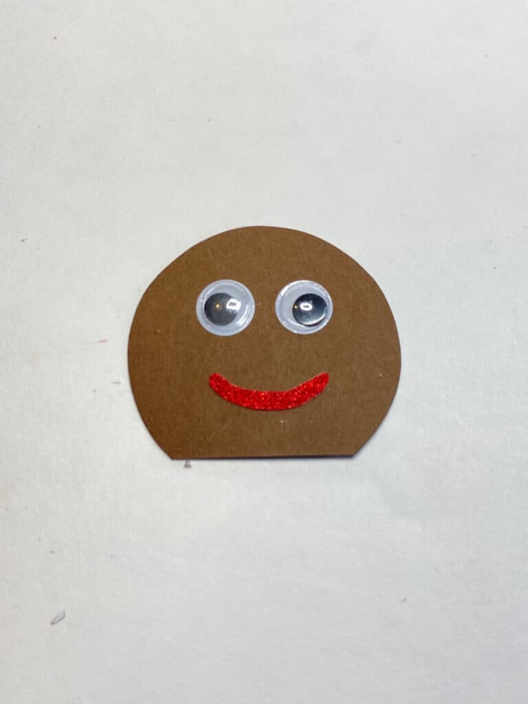 Gingerbread mans head with googly eyes and red smile.