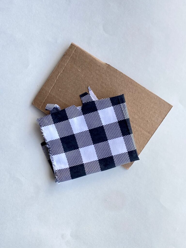 A piece of rectangular cardboard and a piece of black and white buffalo check fabric.
