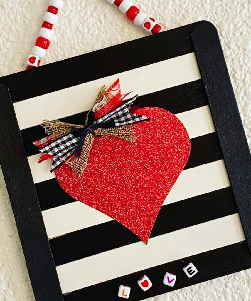 Easy DIY valentine red glitter heart sign made with black and white striped popsicle sticks and lettered Love beads