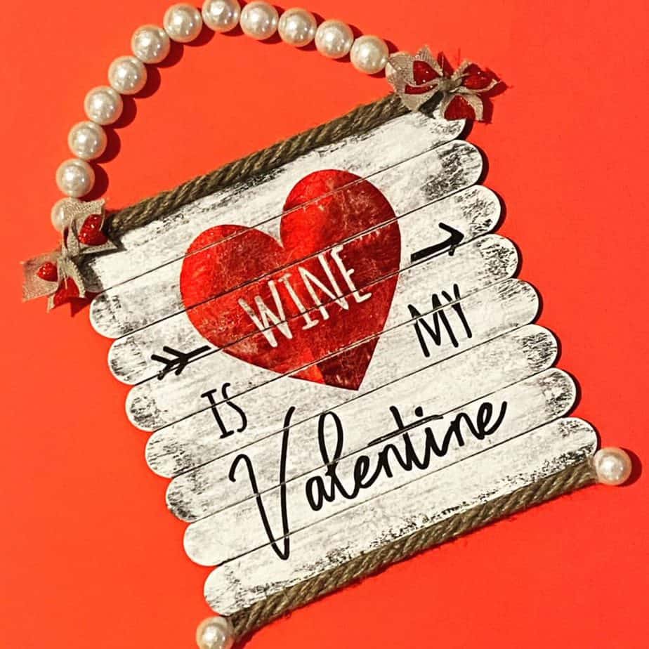 Completed craft project "Wine is my Valentine" DIY Napkin sign made with popsicle sticks for Valentines Day decor with a Pearl Bead hanger.