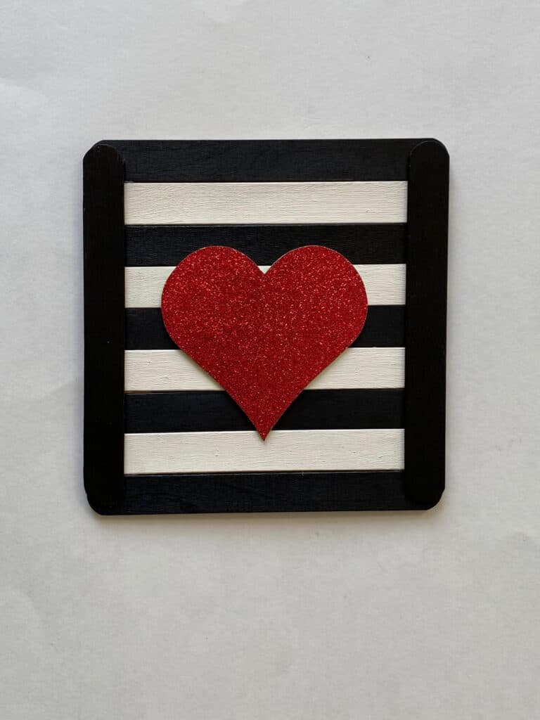 Black and white popsicle sticks glued to together to make a frame with a red glitter heart in the center.