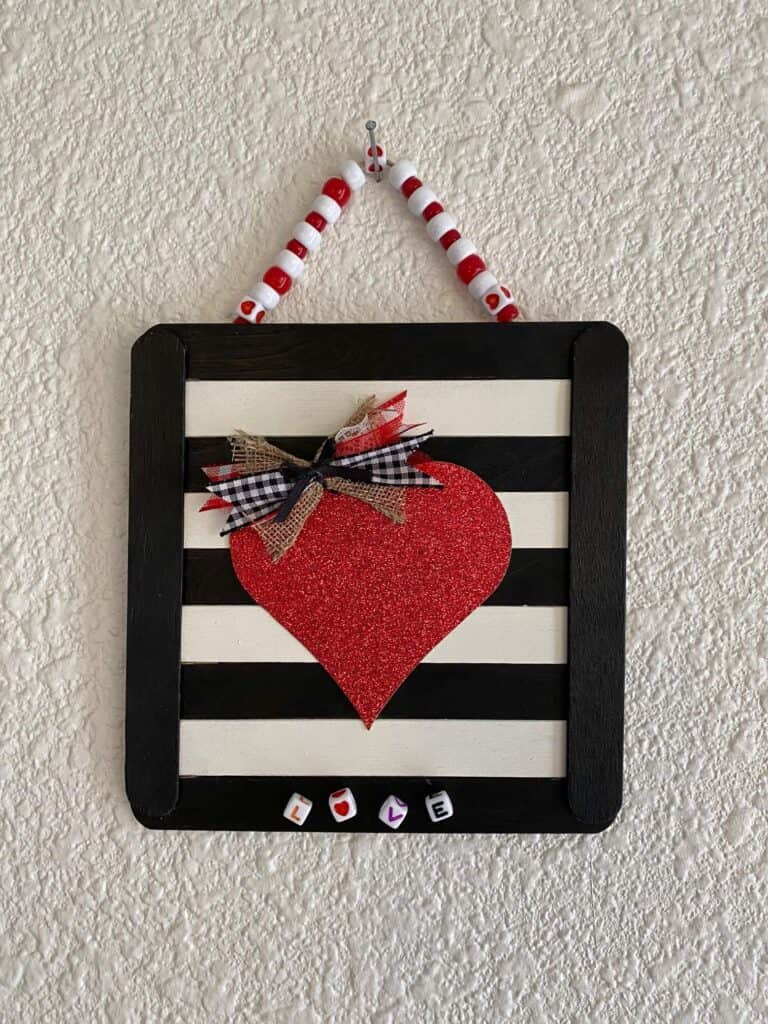 Easy DIY valentine red glitter heart sign made with black and white striped popsicle sticks and lettered Love beads