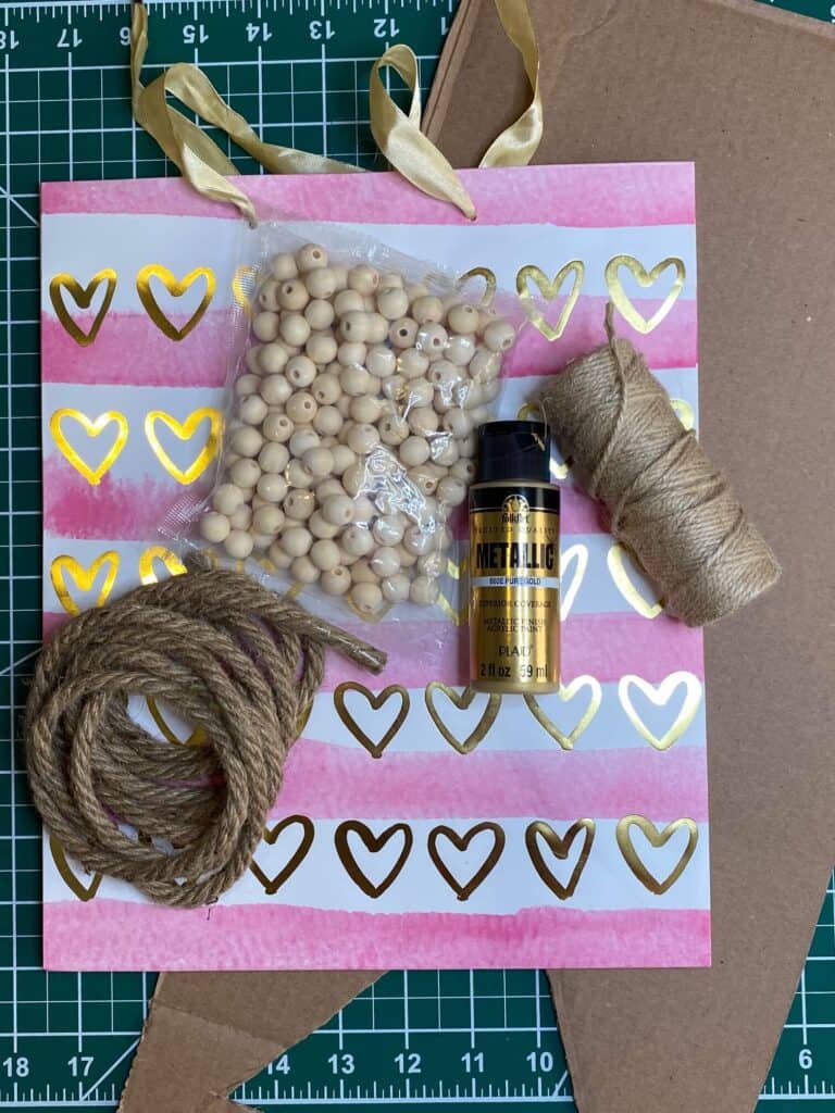 Supplies needed to make a DIY Dollar Tree Valentine Gift Bag Sign with a gold wood bead hanger, and nautical rope.
