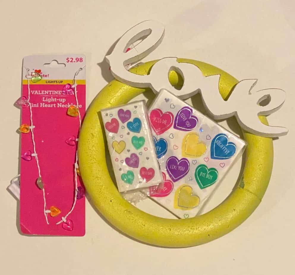 Supplies needed to make a Dollar Tree conversation heart napkin foam wreath for Valentines day with plastic heart necklace and wooden love sign.