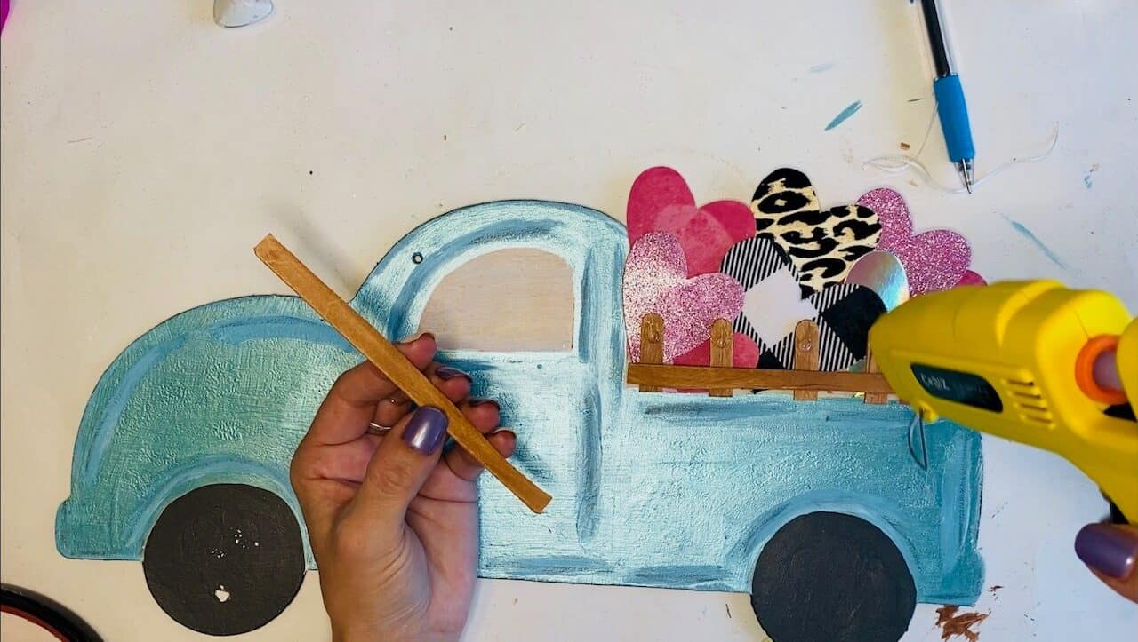 Glue the stained popsicle sticks to the bed of the truck to look like railings holding the hearts inside.