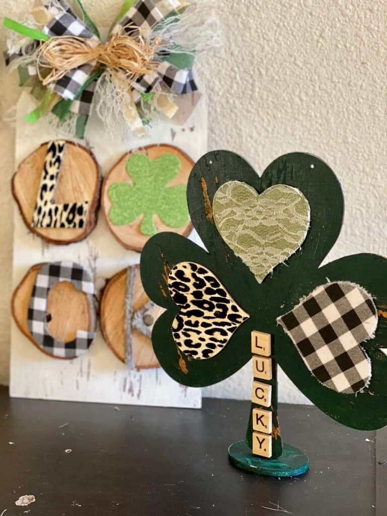 DIY Dollar Tree Wooden Shamrock makeover for a St. Patrick's Day Craft and decor Project, with a rustic door hanger in the background and Leopard print buffalo check word "luck".