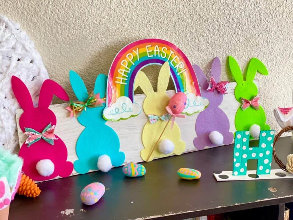 DIY Dollar Tree Rainbow Bunny Sign made from a Banner sitting on a bookcase with other colorful easter decor.