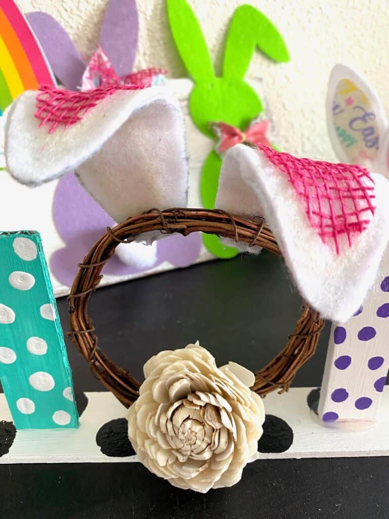 Mini circle grapevine wreath with a faux flower tail and white and pink bunny ears bent flopping backwards.