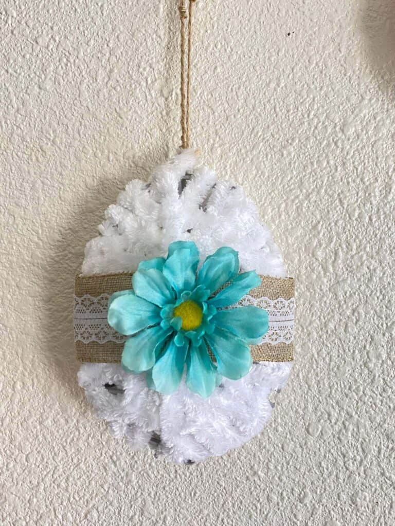 DIY Dollar Tree Tinsel egg makeover. 3D Easter Egg decorated with lace burlap ribbon, a teal faux flower, wrapped with white yarn hanging with a twine hanger.