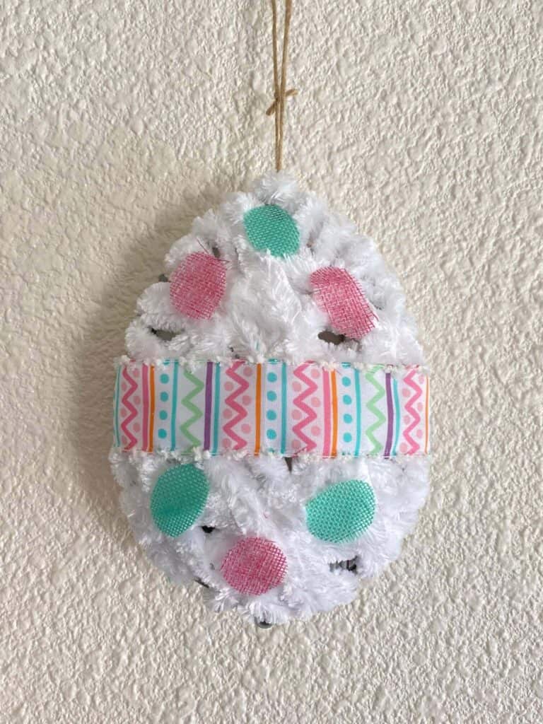 DIY Dollar Tree Tinsel egg makeover. 3D Easter Eggs decorated with pink and teal burlap polka dots and wrapped with white yarn hanging with a twine hanger.