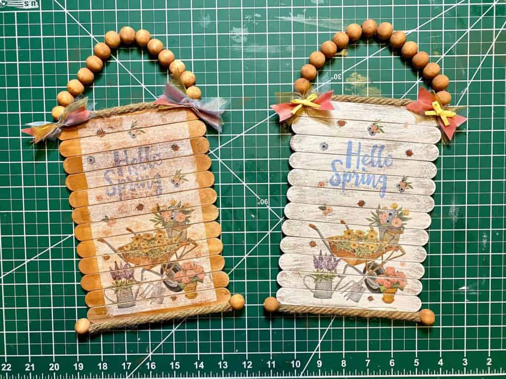 Two completed Hello Spring napkin signs, side by side, one painted white and the other with the popsicle sticks left brown stained.